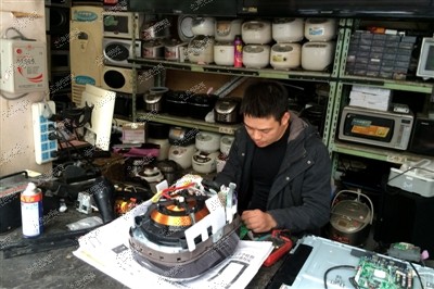 维修店老板贾海涛正在修一款日本的象印电饭煲，他身后堆着十几个类似的进口电饭煲等待维修。晓春 摄